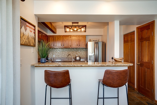 Gather at the breakfast bar and savor your morning coffee in this fully equipped kitchen with warm wood cabinetry, granite counters, and modern appliances ready for your culinary adventures.