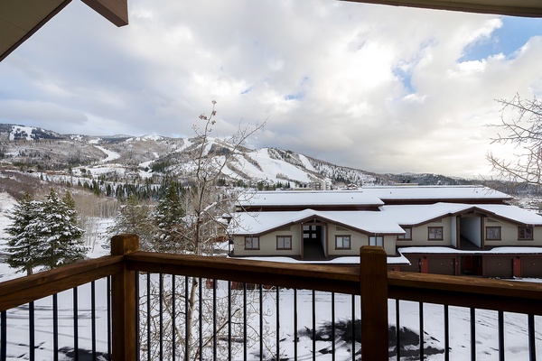 Snow-covered mountains and serene winter landscape visible from the property's balcony, framed by nearby resort buildings and evergreen trees.