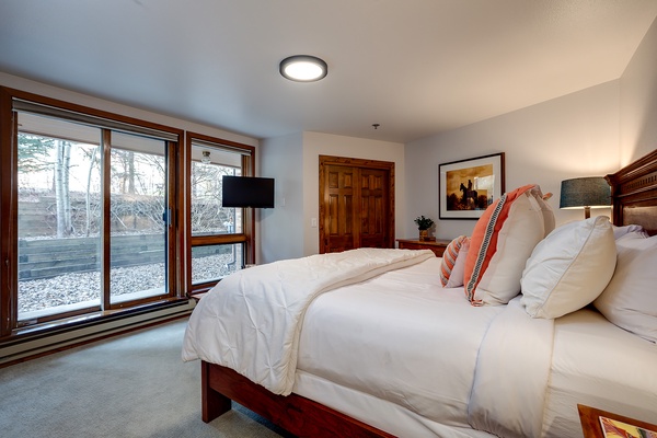 Sink into plush bedding in this serene bedroom where natural light streams through large windows, revealing tranquil outdoor views. Your peaceful mountain escape awaits.