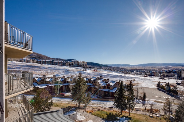 Sweeping winter panorama showcasing snow-covered slopes, neighboring residences, and distant mountain ranges under a brilliant sun. The property is located in a scenic mountain community.