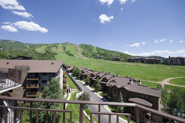A scenic view from the property showcasing the ski slopes, surrounding mountains, and neighboring vacation homes set against a bright blue summer sky.