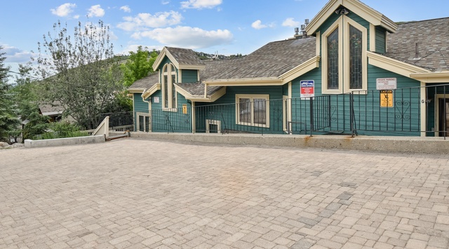 This charming alpine-style building with distinctive green and tan trim sits against a backdrop of lush hillsides, offering convenient access to the surrounding resort area.