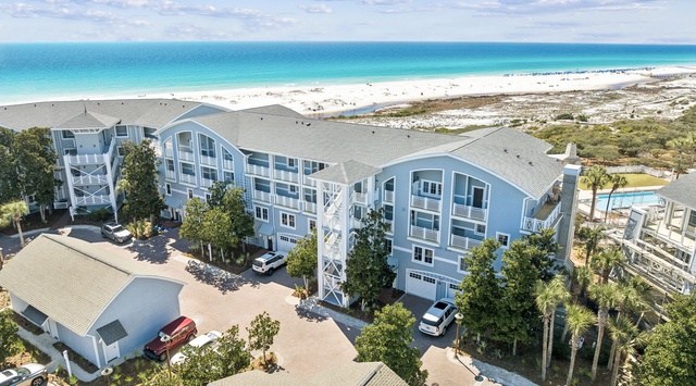 An aerial view showcasing the beachfront property with direct access to pristine white sand and turquoise waters, surrounded by natural coastal vegetation and convenient parking areas.