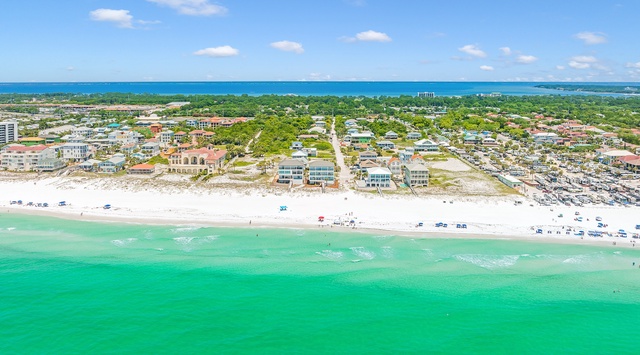 Stunning aerial view of pristine white sand beach with emerald waters and coastal community stretching inland.