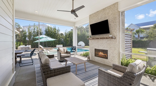 Relax in your covered patio with a cozy fireplace and TV, overlooking the sparkling pool and lush backyard perfect for sunny afternoons.