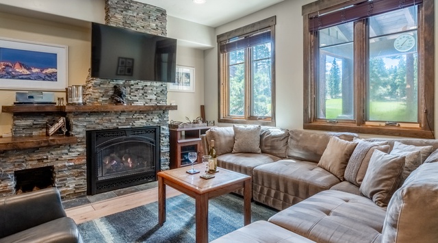Sink into plush seating by your stone fireplace, where large windows frame tranquil views of the surrounding green. The perfect spot to unwind after your adventures.