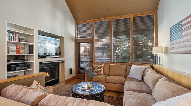 Unwind in your cozy living room with plush sectional seating, warming fireplace, and natural light streaming through wooden blinds.