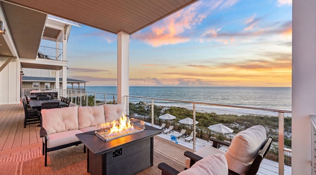 A covered outdoor terrace with a fire table and comfortable seating positioned to capture dramatic coastal sunsets and uninterrupted views of the ocean and surrounding beach landscape.