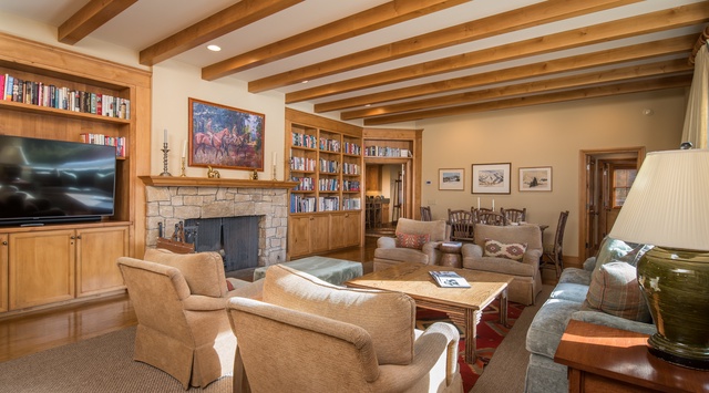Unwind in this elegant living room where exposed wood beams frame your mountain retreat, complete with cozy fireplace and extensive library.