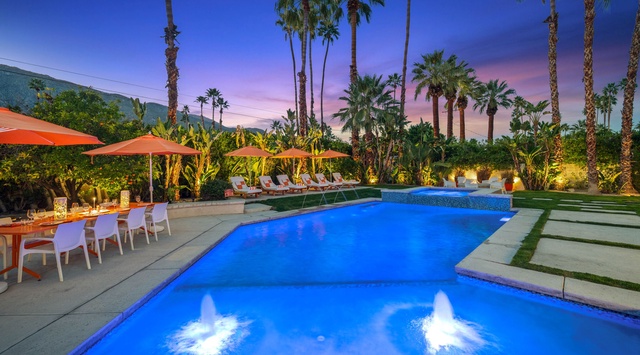 Beautiful pool area surrounded by palm trees with colorful sunset sky in the background.