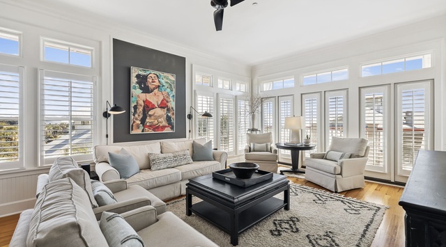 Relax in your spacious living room with plush seating, warm hardwood floors, and abundant natural light streaming through shuttered windows.