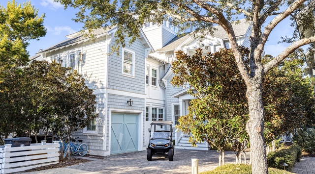 The property is a charming coastal-style home featuring light blue shingle siding, white trim, and mature trees providing natural shade throughout the grounds. Bicycles and a golf cart are available for exploring the surrounding area.