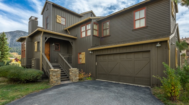 Nestled against a mountain backdrop, this modern home features distinctive architectural charm with its rich earth-toned siding, welcoming wooden accents, and convenient two-car garage.