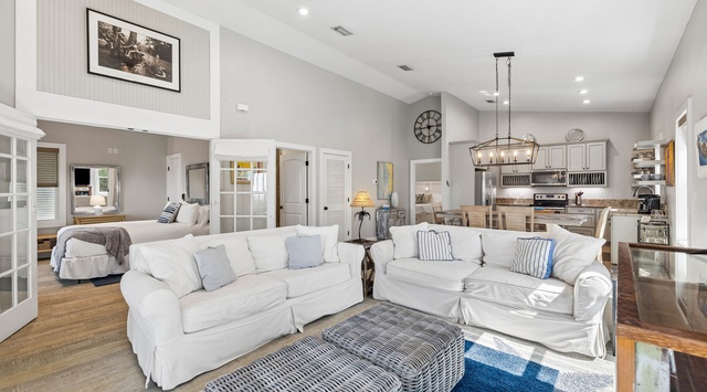 Settle into plush white sofas in your bright, open-plan living space where vaulted ceilings and coastal touches create a welcoming retreat. The kitchen is steps away, perfect for gathering and unwinding.