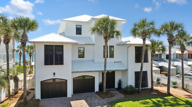 Elegant three-story coastal villa with white metal roof, framed by swaying palms and just steps from the beach—your perfect getaway destination.