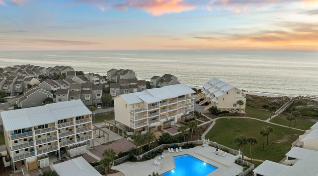 Stunning beachfront property featuring a refreshing swimming pool, surrounded by coastal residences and framed by a pastel-painted sky over the ocean horizon.