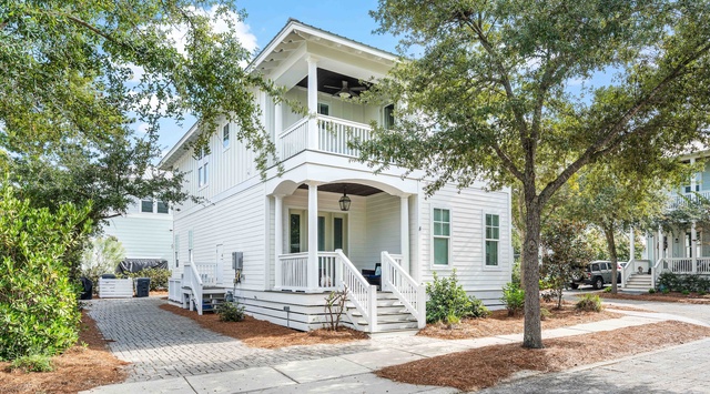 Charming coastal-style home with welcoming front porch and mature oak trees providing natural shade in a peaceful neighborhood setting.