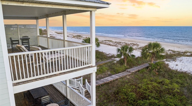 A beachfront property with multi-level decks overlooking white sand, gentle waves, and coastal palms, perfectly positioned to enjoy stunning sunsets over the Gulf.