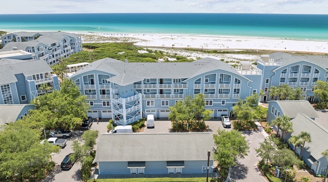 Beachfront resort complex featuring multi-story residential buildings with direct access to pristine white sand beaches and turquoise Gulf waters. The property includes landscaped grounds, parking facilities, and natural dune vegetation.