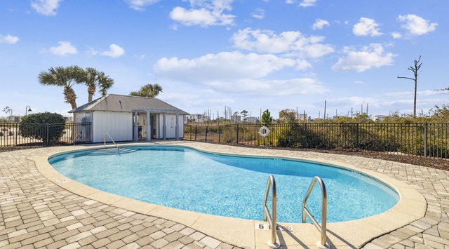 Pristine pool area with paver deck and poolside building, surrounded by coastal palms under bright blue skies.