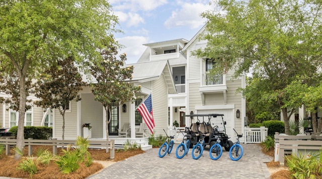 A welcoming coastal retreat with bright blue bikes and a golf cart ready for exploring the neighborhood beneath mature trees and sunny skies.