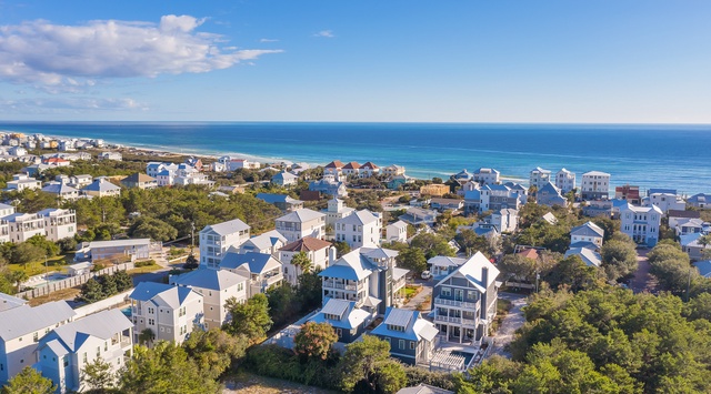 Aerial view of coastal vacation rental community nestled among lush trees, with pristine beach and turquoise waters just steps away.