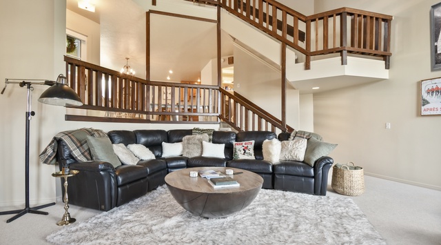 Sink into plush leather seating in your spacious living area, where soaring ceilings and warm wood railings create an inviting mountain retreat atmosphere.