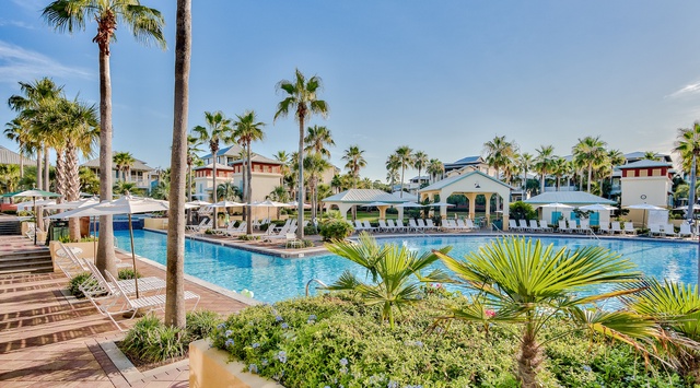 Resort pool area surrounded by swaying palm trees and tropical landscaping with comfortable seating areas.