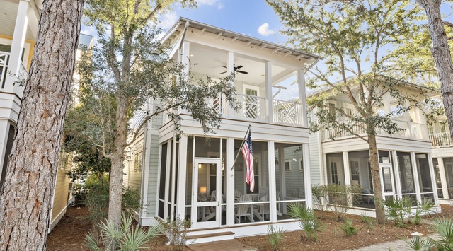 A charming coastal retreat nestled among mature trees with classic architecture and welcoming front porch displaying an American flag.