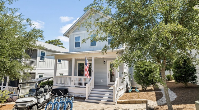 Welcoming coastal-style home nestled among mature trees, complete with a front porch and convenient bikes and golf cart for exploring the surrounding neighborhood.