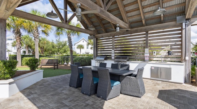 Relax at your covered outdoor kitchen with modern appliances, stylish seating, and tropical palm views for perfect entertaining.