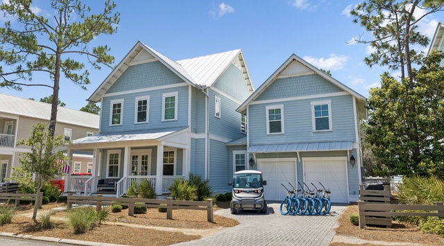 Charming coastal-style home featuring modern blue siding, white metal roofing, and a covered front porch. Bicycles and a golf cart are available for exploring the neighborhood.