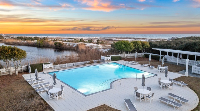 Aerial view of pool and coastal landscape at sunset, with white loungers positioned for relaxation and ocean views beyond the dunes.