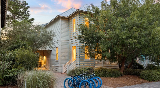 A charming two-story cottage nestled among mature trees, with bicycles ready for exploring the neighborhood at dusk.