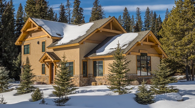 Mountain retreat nestled among snow-covered evergreens, featuring rustic timber architecture and stone accents in a pristine winter landscape.
