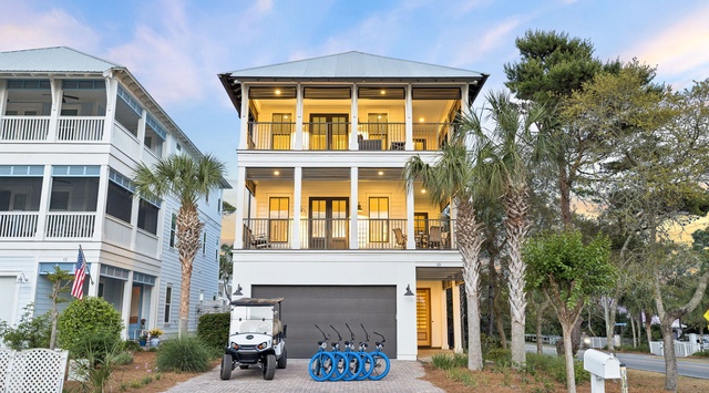 A modern coastal home featuring multiple balconies, garage parking, and complimentary bikes and golf cart for exploring the neighborhood. Surrounded by palm trees in a tranquil residential setting.