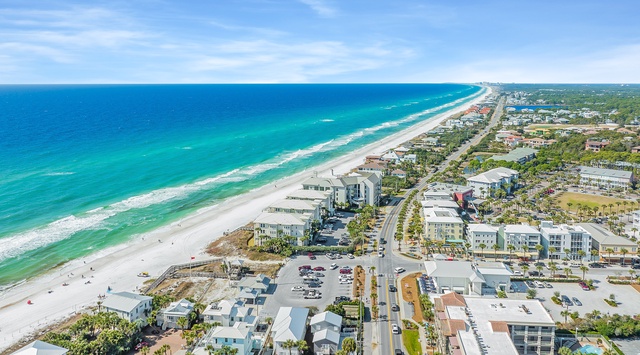 Stunning aerial view showcases pristine white sand beaches meeting turquoise waters, with charming coastal buildings nestled among palm trees.