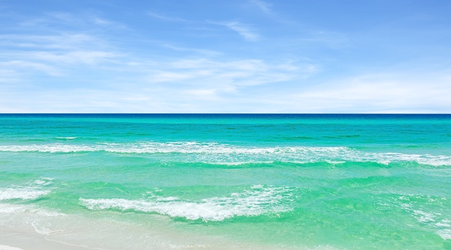 Pristine white sand beach with crystal-clear turquoise waters and gentle waves under a brilliant blue sky.