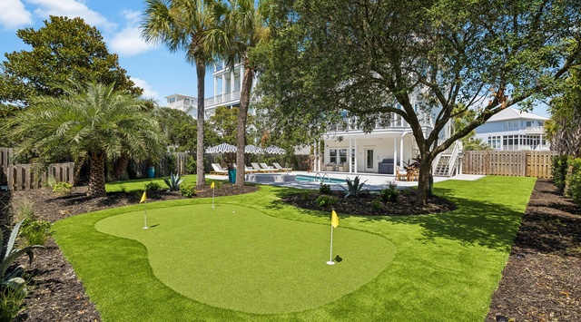 The property features a private putting green surrounded by lush landscaping and tall palms, with a sparkling pool and spacious outdoor seating areas perfect for relaxing under the coastal sun.
