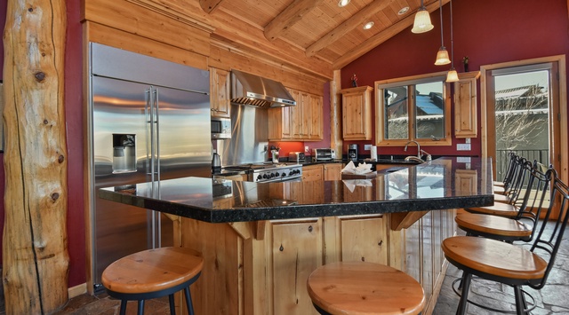 Gather around this stunning kitchen island where culinary adventures await, featuring granite countertops and stainless steel appliances under soaring wood beam ceilings.