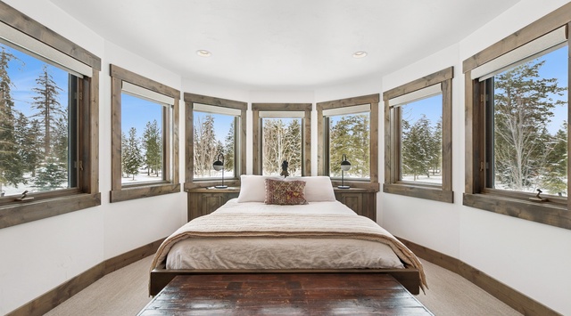 Wake up surrounded by panoramic winter views in this dreamy bedroom where floor-to-ceiling windows frame the snowy landscape.