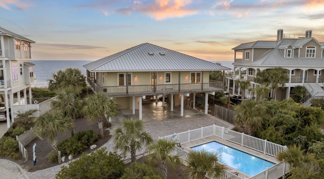 Coastal retreat showcasing elevated beach house architecture with private pool surrounded by lush palm trees, positioned between ocean and neighboring properties.