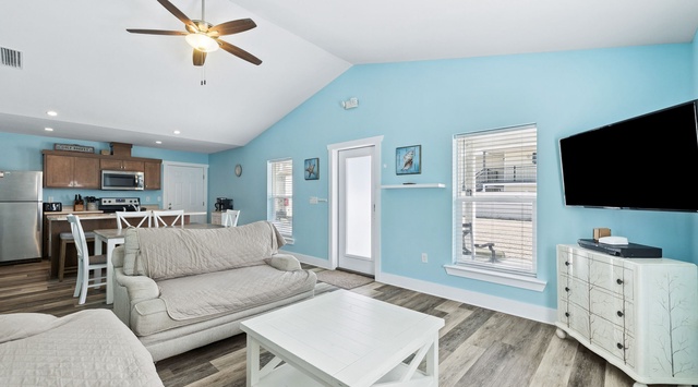 Relax in your bright, coastal-inspired living space with soft blue walls, comfortable seating, and modern amenities for your perfect getaway.