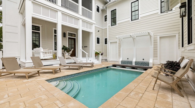 Your private courtyard retreat features a sparkling pool surrounded by elegant loungers and cozy seating, all framed by bright white architecture and warm natural light—perfect for unwinding in style.