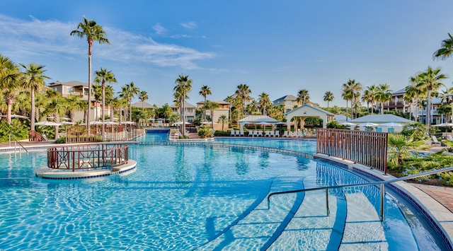 Resort-style swimming pool surrounded by tropical palm trees and vacation homes in a beautiful sunny setting.