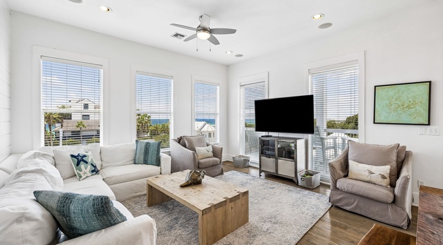 Sink into plush seating and let the coastal breeze flow through. Your living space glows with natural light from multiple windows, offering glimpses of the sea beyond—your perfect spot to unwind after a day of beachside adventure.
