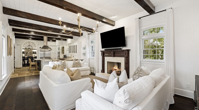 Sink into plush white sofas beside your crackling fireplace, where rustic beams meet elegant comfort in this stunning open living space.