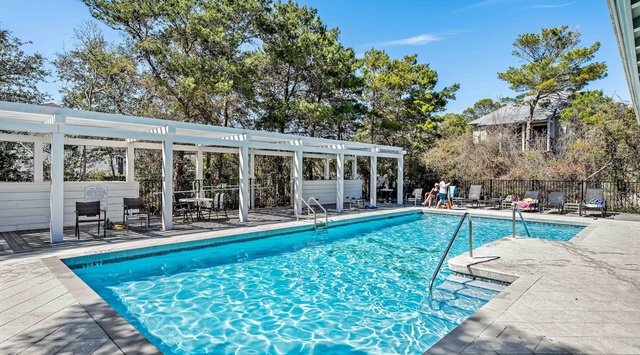 A sparkling outdoor pool surrounded by tall pines and a white pergola, perfect for sunny afternoons. Lounge chairs and poolside seating let you relax in the shade or soak up the warmth.