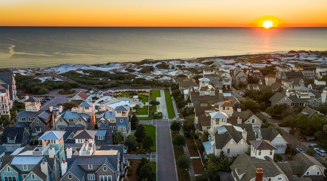 Stunning aerial perspective of a charming beachside community at golden hour, with colorful homes nestled between coastal dunes and pristine shoreline.
