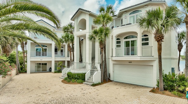 Elegant coastal home featuring Mediterranean-style architecture with tropical landscaping and spacious brick-paved driveway.